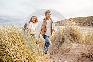 Three Children Having Fun Exploring In Sand Dunes On Winter Beach Vacation