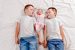 Three children lie on their backs on white sheet. Two older brothers and a newborn baby girl