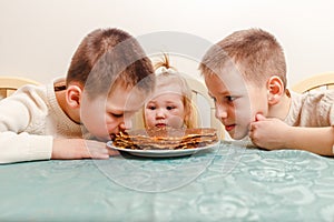 Three children and plate of pancakes for the carnival. kids eat pancakes at home at the table