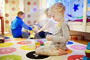Three children playing with colorful plastic blocks at kids room. Cute girl playing at home or daycare.