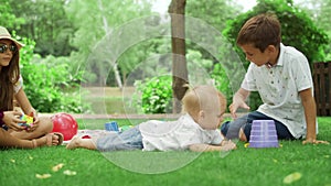 Three children playing with toys in park. Toddler lying on green grass outside