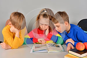 Three children read a book and do their homework assigned at school