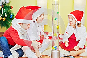 Three children in santa caps sit on fur rug and
