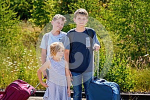 Three children, school boys and preschool girl with suitcases before leaving for summer vacation camp. Happy kids