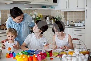 Three children, sibling brothers, painting easter eggs for decoration, mom helping them