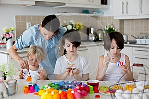 Three children, sibling brothers, painting easter eggs for decoration, mom helping them