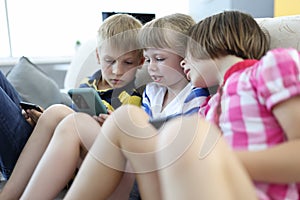 Three children sit on couch and hold telephone.