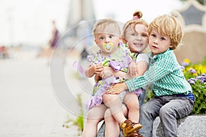 Three children sit embracing on granite curb of