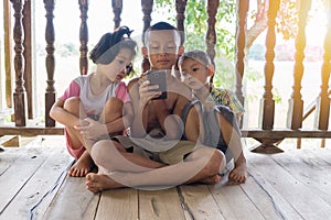 Three children sit and watch the smartphone happily. young boys and girls with cellphone communication. on the terrace of their