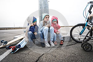 Three children skated on a skateboard and a bicycle and sat down to rest on the curb.