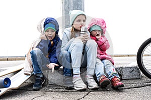 Three children skated on a skateboard and a bicycle and sat down to rest on the curb.