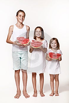 Three children in the studio stand on a white background and hold pieces of watermelon