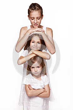 Three children in the studio on a white background, a brother and two sisters, put their hands on each other `s head, stand the t