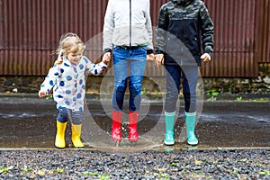 Three children, toddler girl and two kids boys wearing red, yellow and green rain boots and walking during sleet. Happy