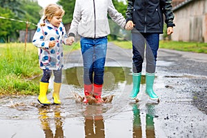 Three children, toddler girl and two kids boys wearing red, yellow and green rain boots and walking during sleet. Happy