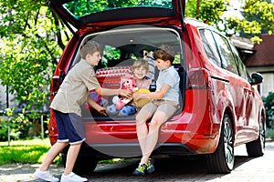 Three children, two boys and preschool girl sitting in car trunk before leaving for summer vacation with parents. Happy