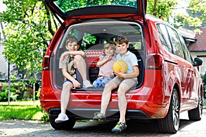 Three children, two boys and preschool girl sitting in car trunk before leaving for summer vacation with parents. Happy