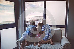 Three children watching sunrise on terrace or balcony. Two kids boys and preschool girl watch sun on horizon. Happy