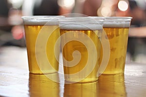 Three chilled cups of beer on a wooden surface in an outdoor biergarten.