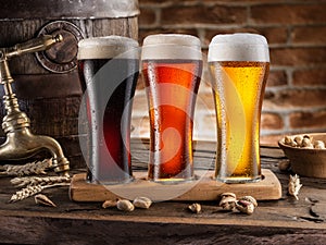 Three chilled glasses of different beer and beer barrel on wooden table closeup