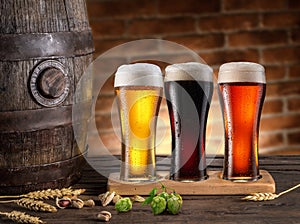 Three chilled glasses of different beer and beer barrel on wooden table closeup