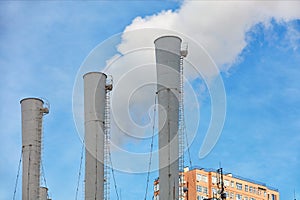 Three chimneys of a thermal power plant emitting steam under a clear blue sky against the backdrop of the top of a residential