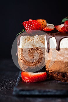 Three chocolates cake with chocolate drips on a black background. Layered cake with milk, black and white chocolate souffle