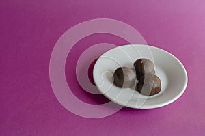 Three chocolates in a white porcelain saucer on a pink background