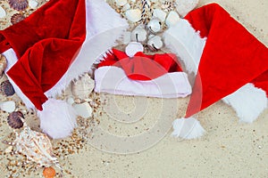 Three christmas hats on the beach. Santa hat the sand near shells. Family holiday. New year vacation. Copy space. Frame. Top view