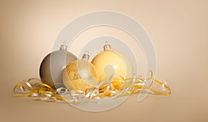 Three Christmas New Year balls of gray gold and yellow lie near a serpentine on a yellow beige background.