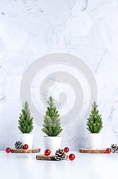 Three christmas tree with pine cone and decor xmas ball on white table and marble tile wall background.clean minimal simple style.