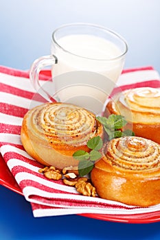 Three cinnamon rolls and jug of milk on red plate