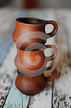 Three clay ceramic cups on top of each other. Handmade pottery. Wooden background