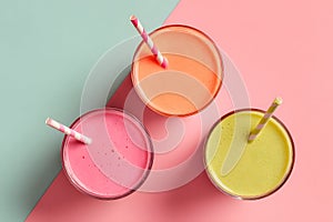 Colorful drinks in clear glasses with straws on a pink and blue background during daytime