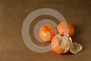 Three clementines on brown paper, one half-peeled