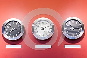 Three clocks on red wall showing different time