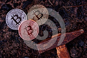 Three coins of bitcoin on black earth and a hammer