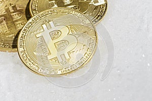 Three coins of crypto-currency bitcoin lie on white snow.