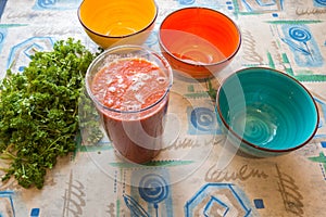 Three colored bowls next to greenery and jug of tomato juice