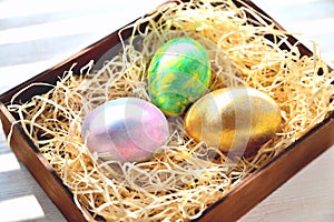 Three colored chicken eggs in a box with shavings in the sunlight