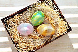 Three colored chicken eggs in a box with shavings in the sunlight