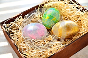 Three colored chicken eggs in a box with shavings in the sunlight