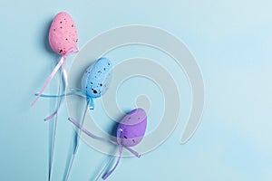 Three colored decorative Easter eggs on sticks with ribbons on light blue background. Easter festive background