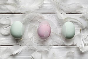 Three colored eggs and white feathers on wooden table