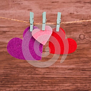Three colored hearts hanging thread on wooden background