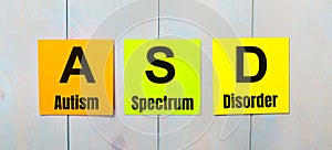 Three colored stickers with the text ASD Autism Spectrum Disorder a light blue wooden background