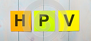 Three colored stickers with the text HPV on a light blue wooden background