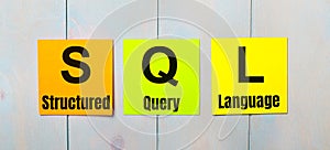 Three colored stickers with the text SQL Structured Query Language a light blue wooden background