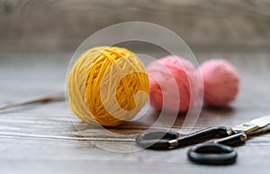 Three colored wool balls, knitting needles and scissors on the wooden background