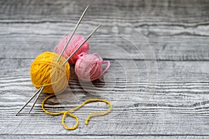 Three colored wool balls, knitting needles on the wooden background